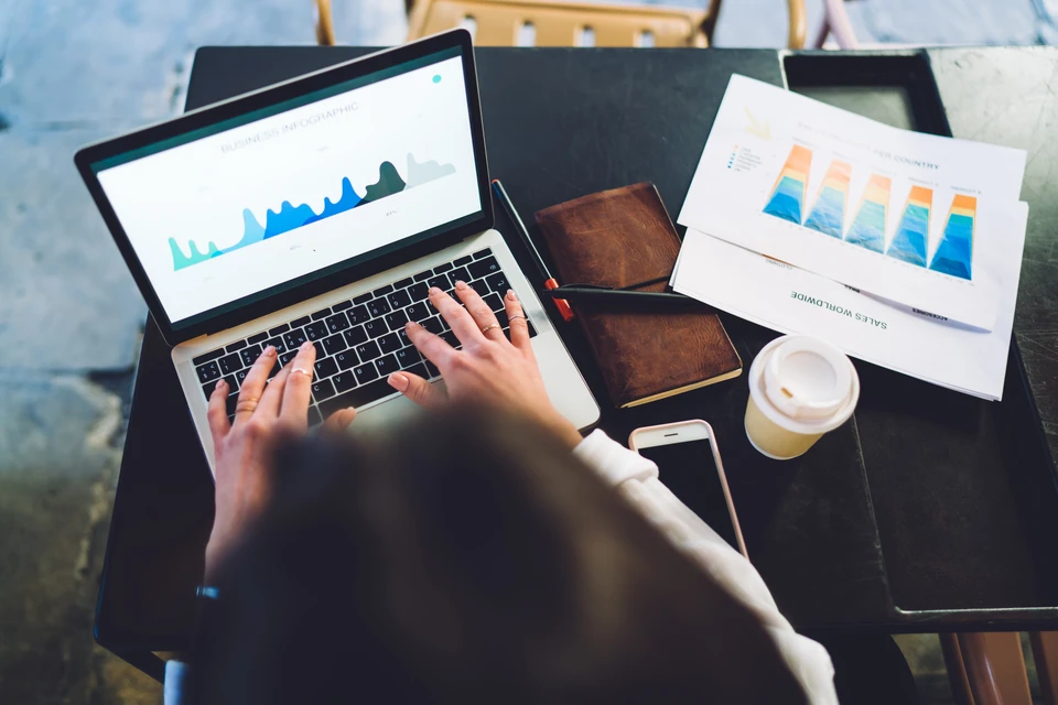 Personne travaillant sur ordinateur portable dans un environnement professionnel, consultant des graphiques et donn&eacute;es analytiques &agrave; l'&eacute;cran