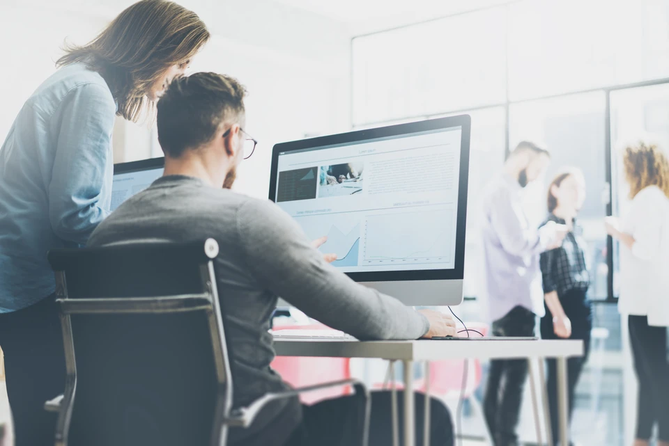 Espace de travail moderne avec deux professionnels analysant des données sur écran d'ordinateur