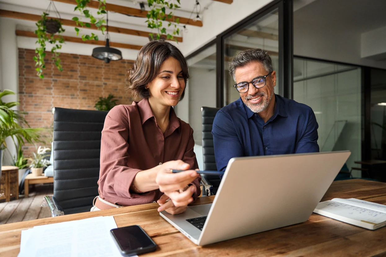 Équipe de quatre professionnels collaborant dans bureau moderne lumineux, analysant données sur ordinateur portable et documents