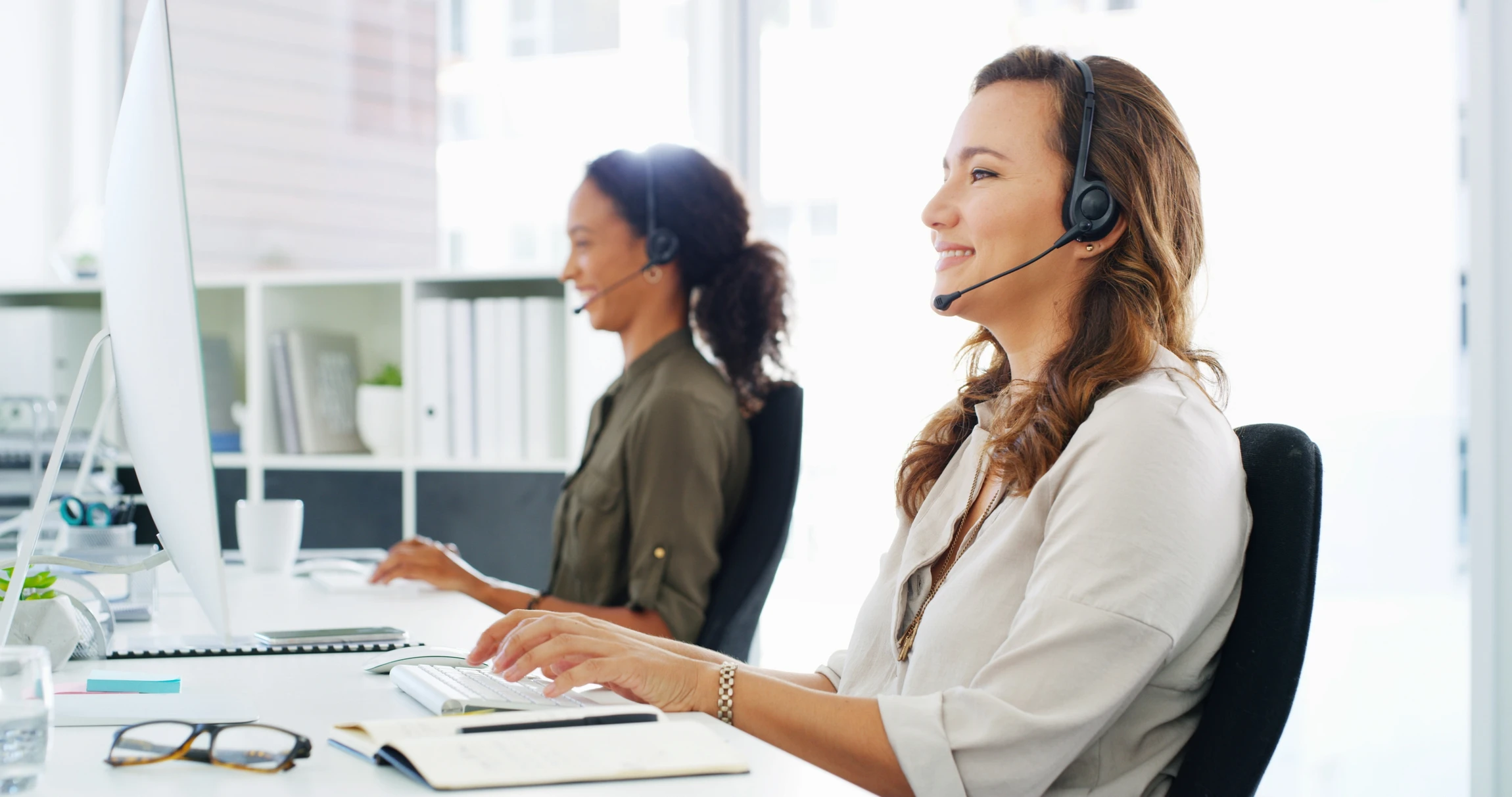 Espace de travail moderne avec trois employés en costumes sombres équipés de casques-micros, assis à des postes informatiques
