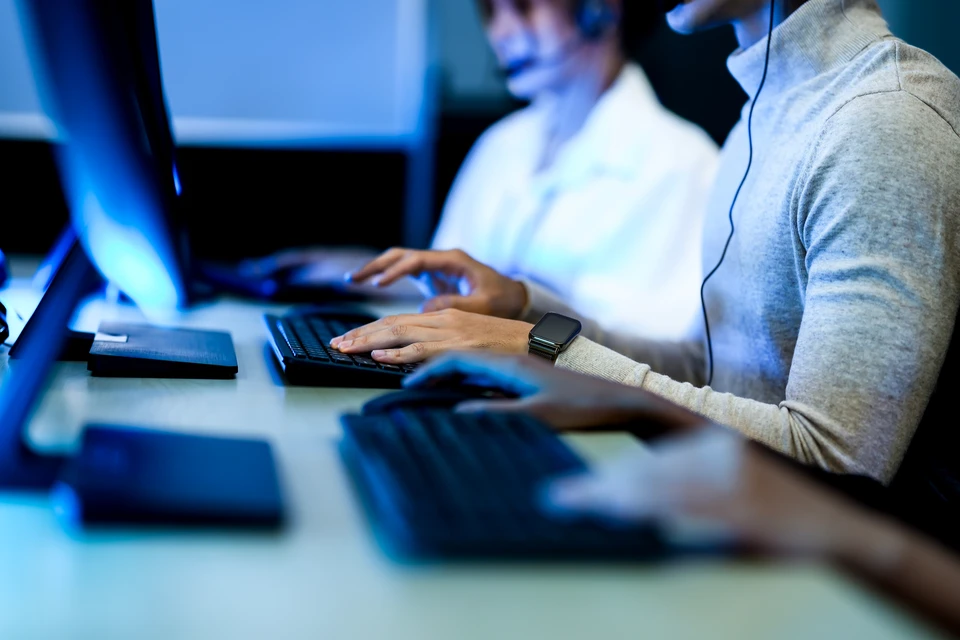 Technicien informatique dans un bureau moderne, assis à son poste de travail équipé de plusieurs écrans, en train de se connecter à distance sur les équipements d'un client, avec une expression concentrée montrant l'engagement actif dans la résolution de problème informatique. L'image doit clairement montrer le contexte de travail à distance (écrans, connexion) plutôt qu'une équipe générique, pour transmettre l'idée d'intervention immédiate sans déplacement.